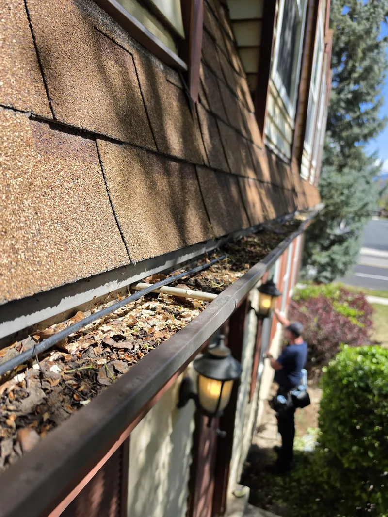 Gutter cleaning in West Jordan, Utah — Ember technician clearing leaves and debris from a home's gutters