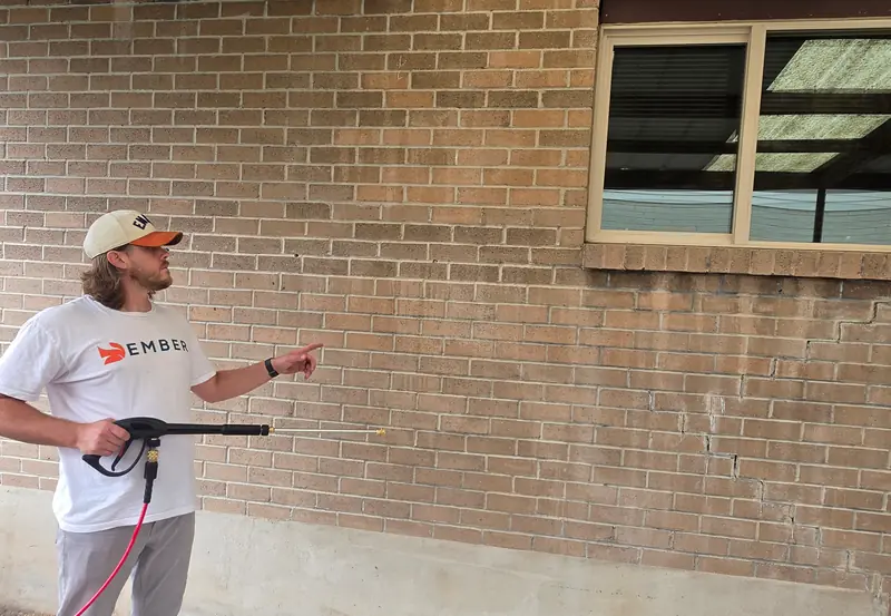 Pressure washing in Salt Lake City — Ember technician sizing up a brick exterior with a pressure washer